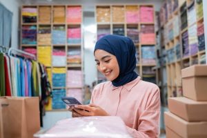 happy-young-female-seller-using-phone-while-sitting-desk_8595-30478